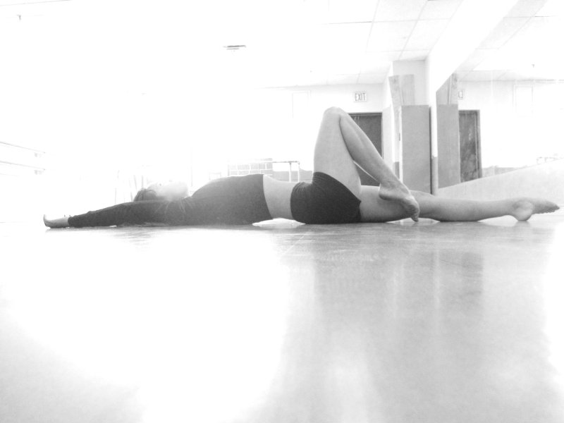 Dancer stretches on floor, light behind